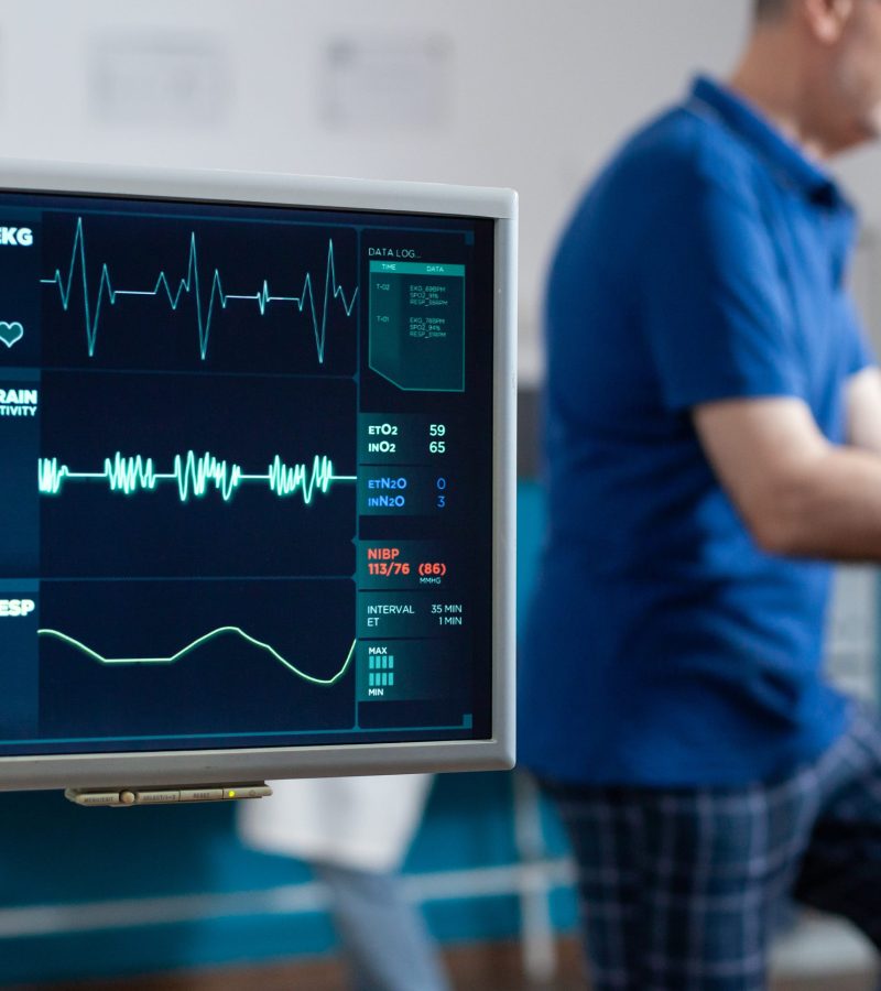 Close up of heart rate monitor measuring pulse while patient doing exercise for physical recovery. Senior man using stationary equipment to recover with physiotherapy and gymnastics.